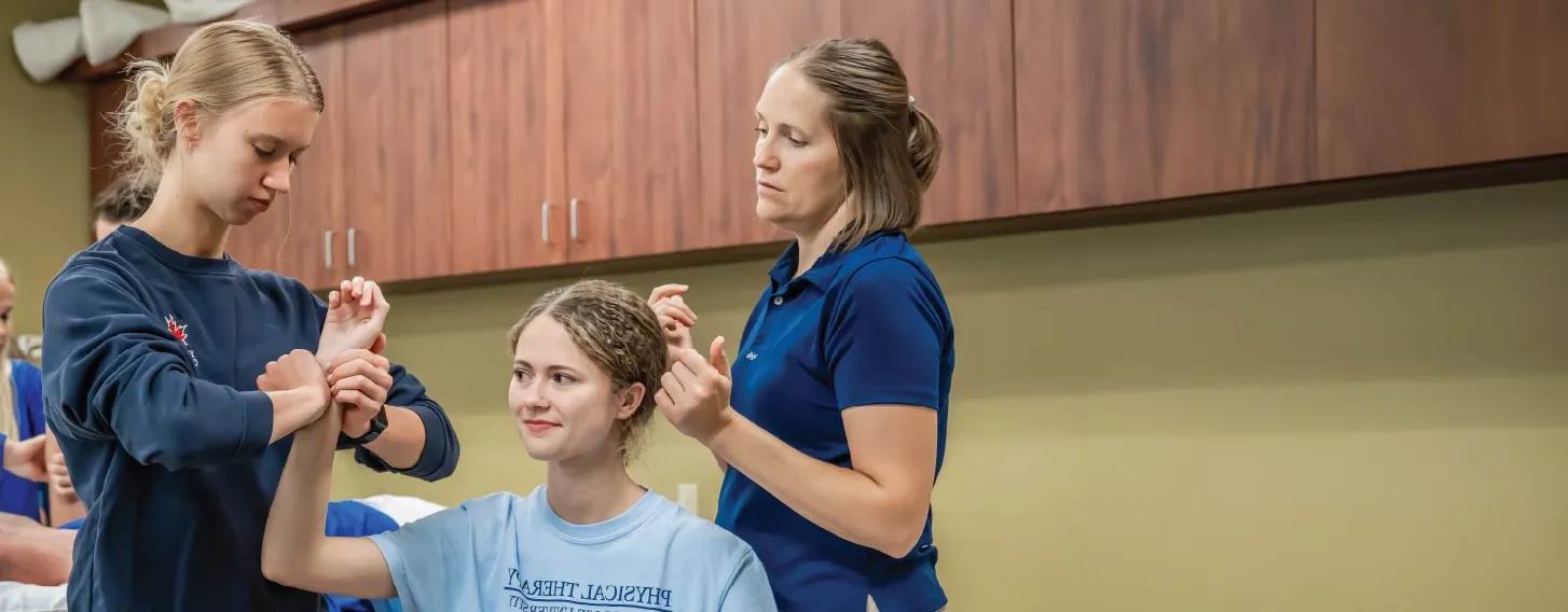 Student and teacher examining patient in physical therapy lab.